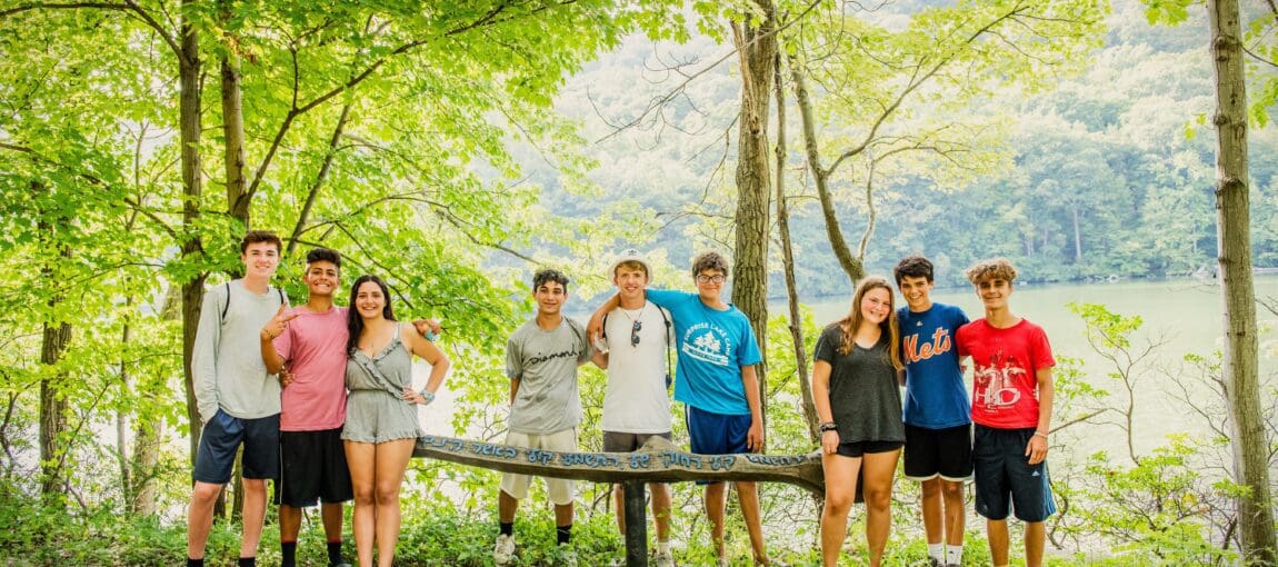 Teen SLC campers pose inn the woods, next to a wooden bench.